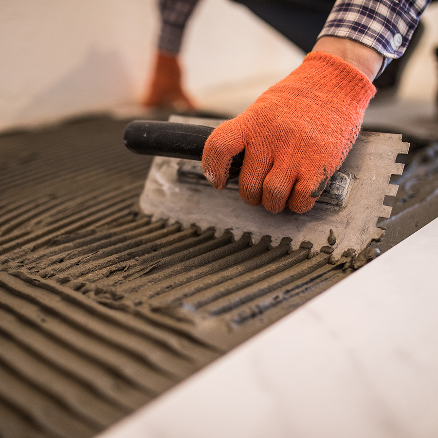Laying Ceramic Tiles. Troweling mortar onto a concrete floor in preparation for laying white floor tile. Laying Ceramic Tiles. Troweling mortar onto a concrete floor in preparation for laying white floor tile.